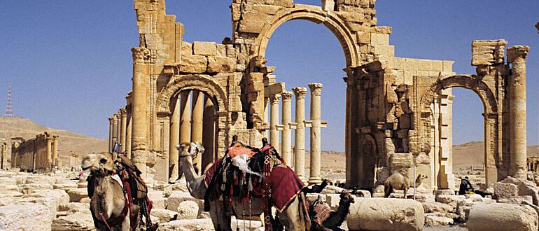 Reitkamele vor dem Monumentalbogen der Säulenstraße in Palmyra