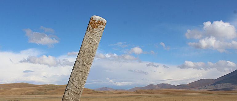 Geneigter Hirschstein vor Dutzenden von kleinen Steinhügeln, den Gräbern rituell geopferter Pferde an der bronzezeitlichen Monumentalstätte Ikh Tsagaanii Am, Provinz Bayankhongor, Zentralmongolei